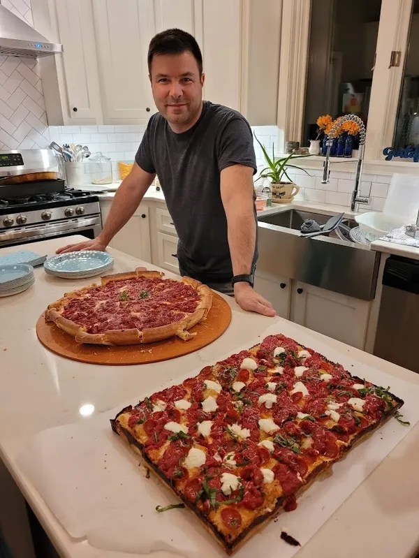 Bill smiling in his kitchen with two homemade pizzas on the counter